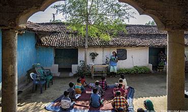 Un grupo de estudiantes de primaria atiende durante una sesión informativa sobre la COVID-19 en el patio de una escuela en India.