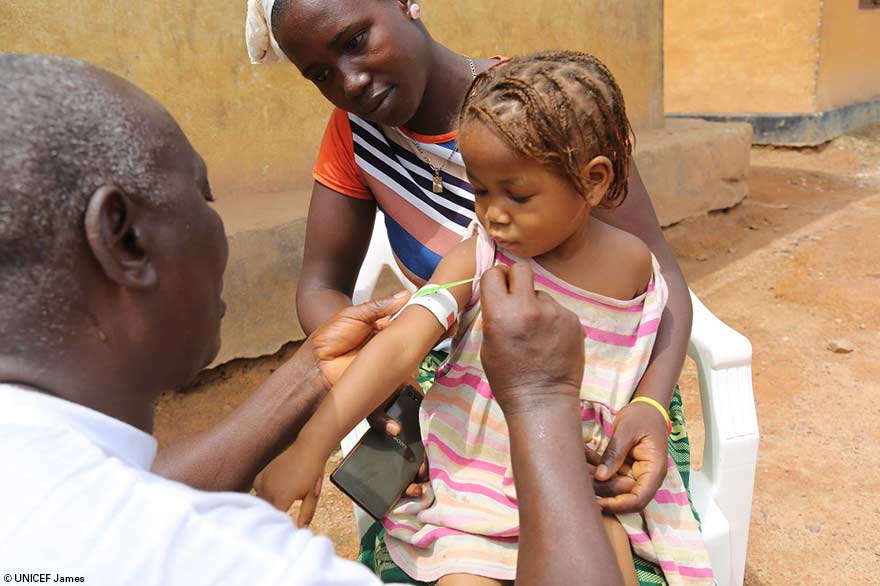 Un trabajador de salud mide el brazo de Hawa Kaba, 3, mientras su madre, Isatu Kaba, observa