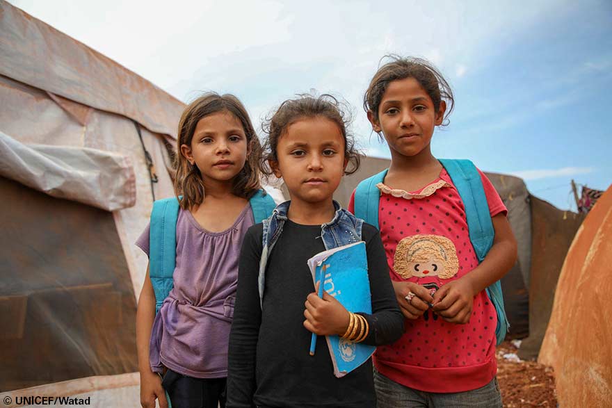 Niñas con mochilas de UNICEF se ubican frente a una tienda de campaña donde 350 niños de entre 7 y 14 años vuelven a aprender.