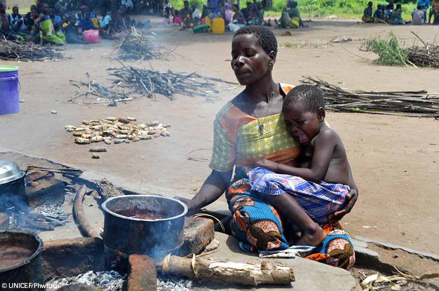 Eneless Bernard prepara una comida en el campamento de la escuela primaria de Chagambatuka en Chikwawa mientras su hija de 3 años, Lincy llora en los brazos de su madre.