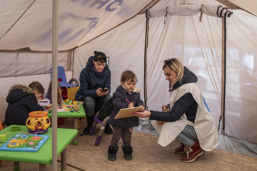 Una psicóloga infantil habla con un niña de 3 años y otro de 7 en una tienda de campaña de UNICEF. 