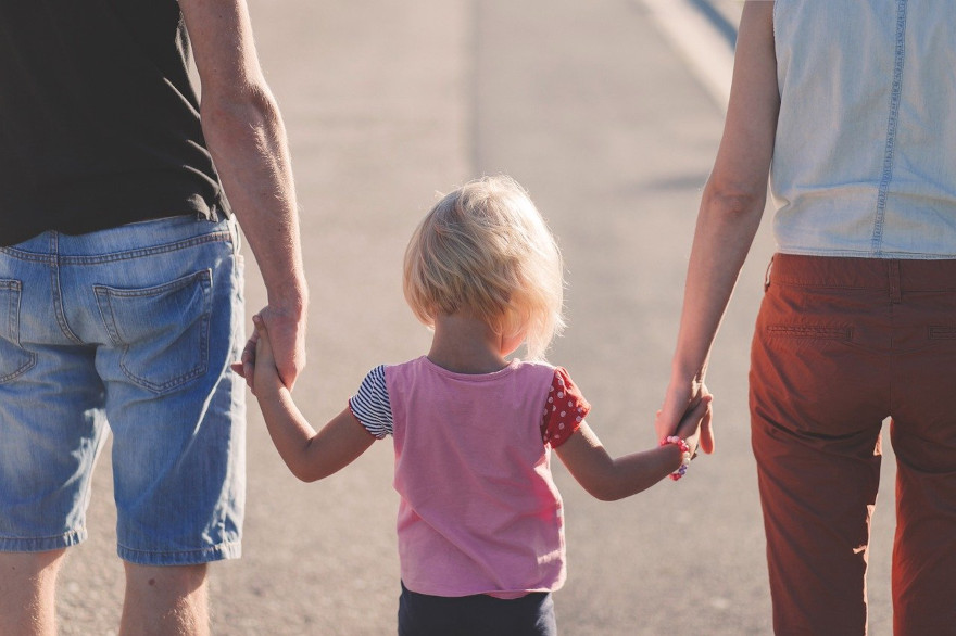 Una niña camina de la mano de su familia.