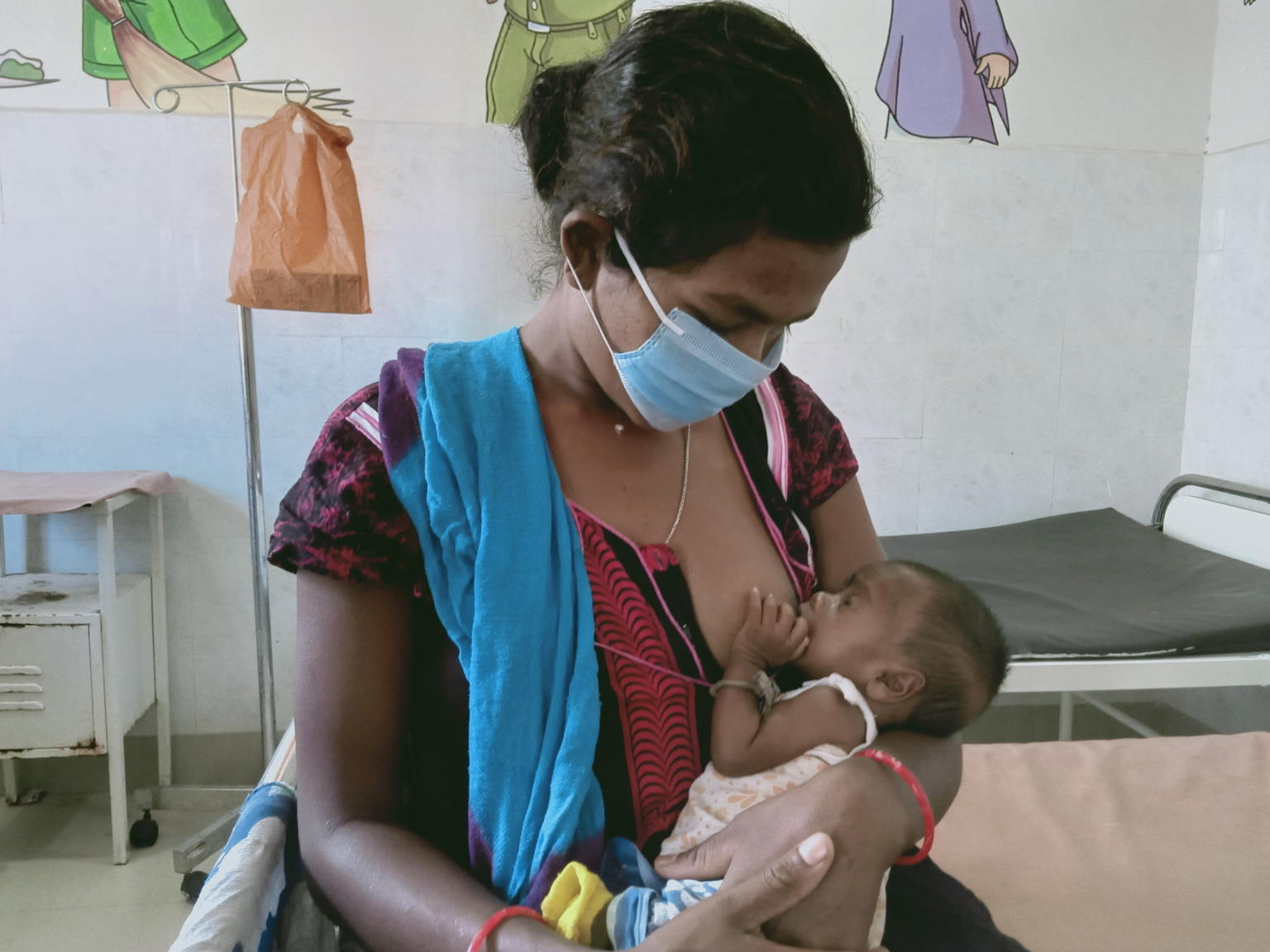 Una madre da el pecho a su bebé con mascarilla en India