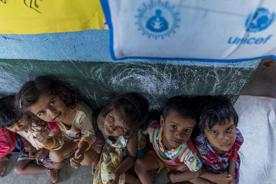 Unos niños y niñas sentados junto a una pared en un centro infantil de UNICEF en India.