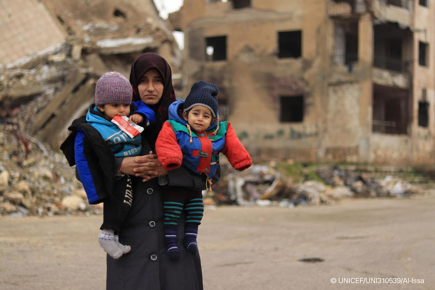 Una madre sostiene en brazos a sus dos hijos en Siria.