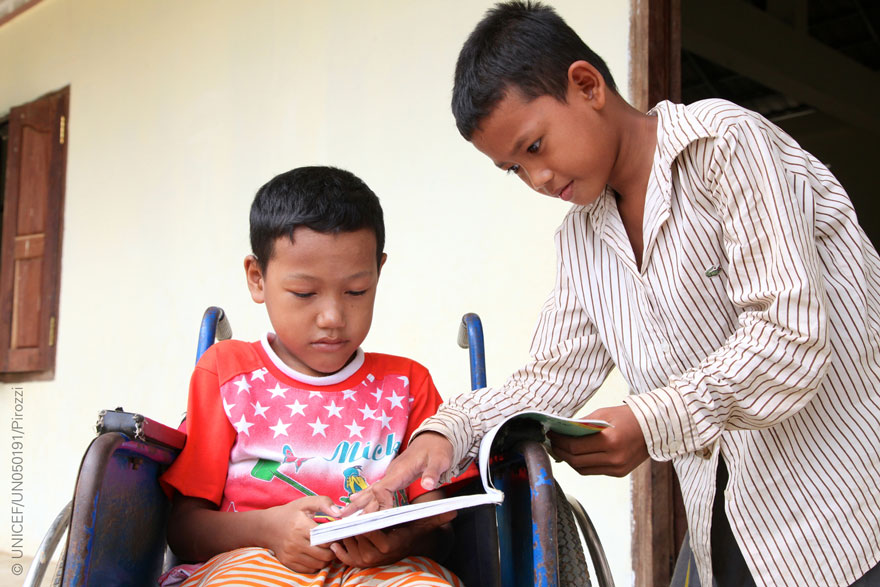 Un niño con discapacidad comparte un libro con un amigo en su escuela de Camboya.