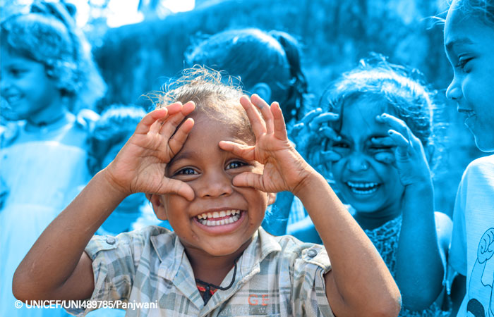 Niña sonriente jugando con sus manos como si llevara unas gafas imaginarias.