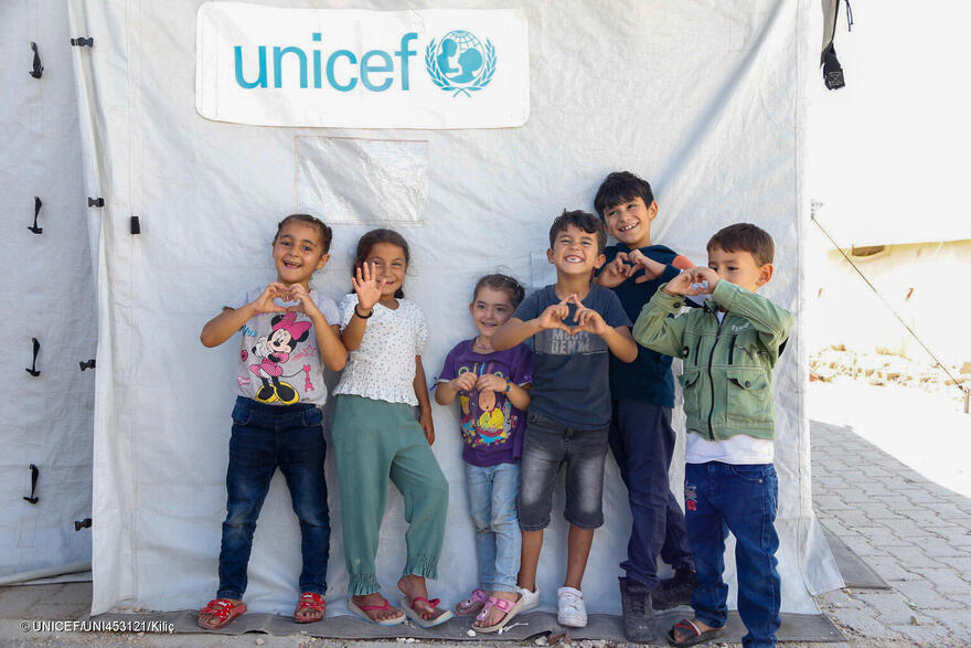 Un grupo de niños frente a un aula en una tienda de campaña apoyada por UNICEF en un campamento informal de Hatay, Turquía