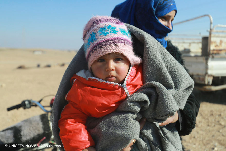 Una niña pequeña sonríe mientras su madre espera recibir el kit de invierno de su familia, distribuido por UNICEF