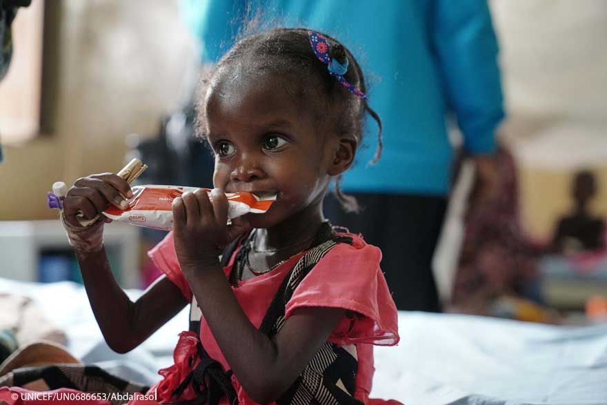 Una niña toma un sobre de alimento terapéutico en Sudán