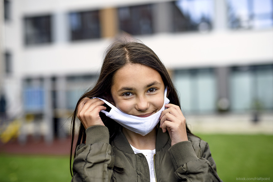 Una niña sonríe mientras se pone una mascarilla