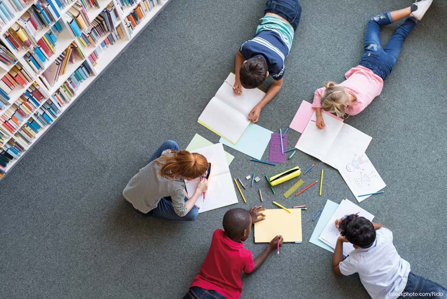 Un grupo de niños y niñas dibujan en el el suelo de una biblioteca