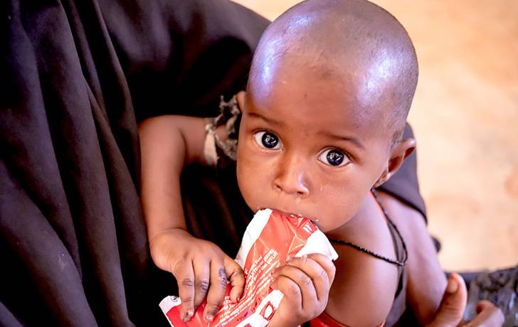 Alerta por hambre: El tiempo se acaba. Ayúdalos. Un bebé come alimento terapéutico.