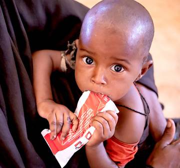 Alerta por hambre: El tiempo se acaba. Ayúdalos. Un bebé come alimento terapéutico.