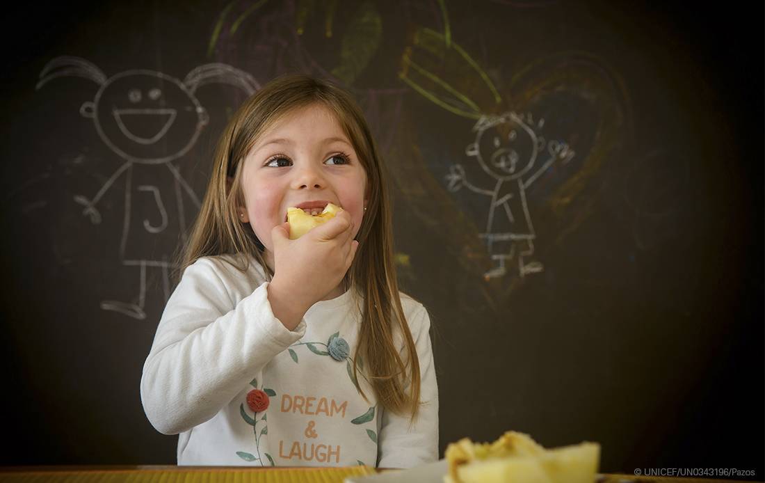 Una niña come una manzana en un aula