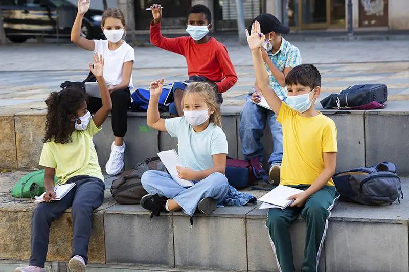Un grupo de niños y niñas alzan la mano para participar en una clase al aire libre